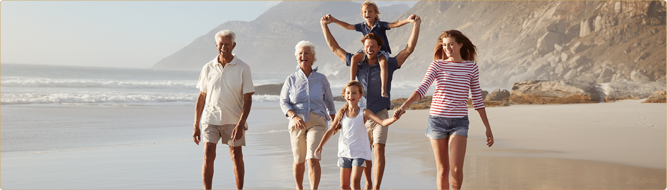 Multi Generation Family On Vacation Walking Along Beach Together