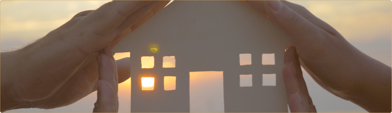 Group of human palms on all sides of a cut out house diagram with setting sun coming through window over water